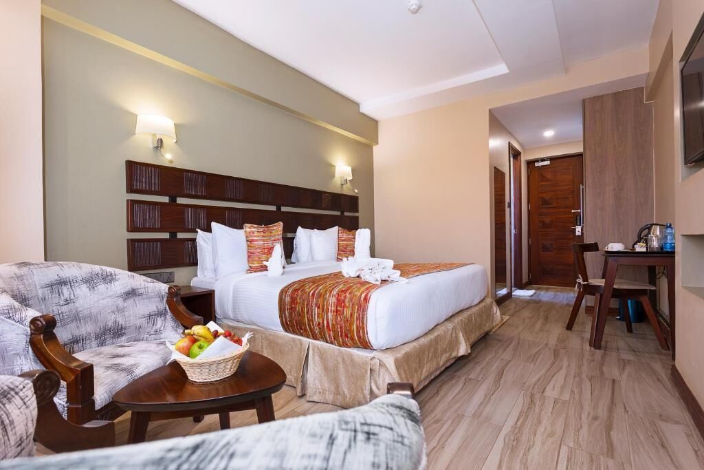 A hotel room with a bed, a sofa, a small table with fruit, and a desk with a chair.