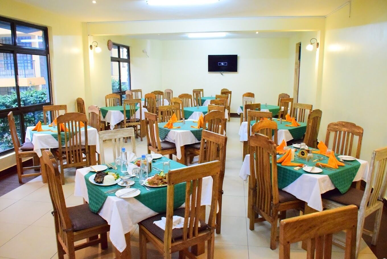A dining area with multiple tables, chairs, and a television screen on the wall.