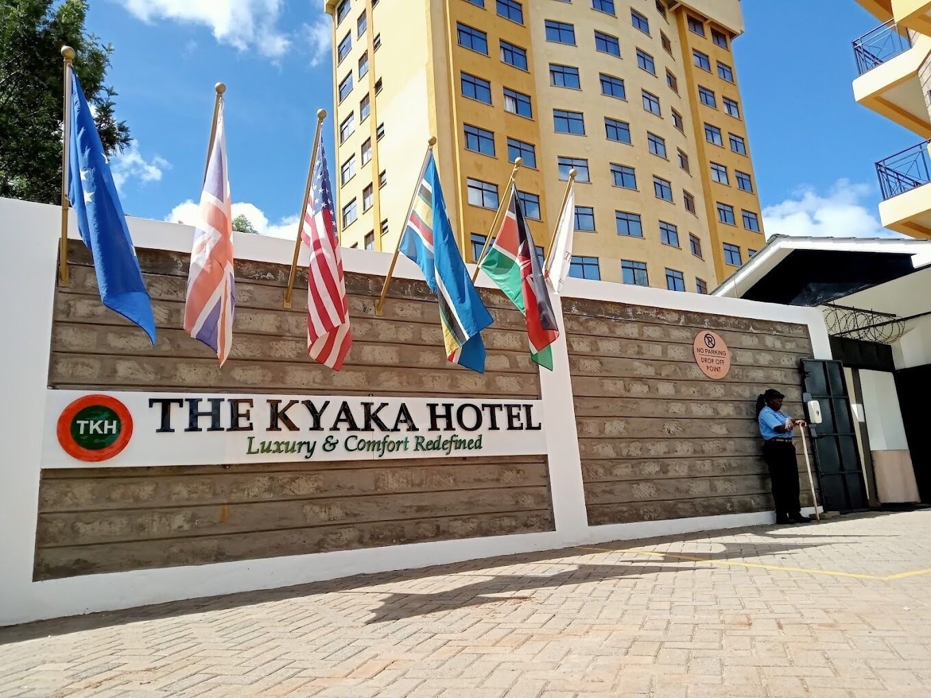 The Kyaka Hotel with multiple flags, a sign indicating no parking, and a security guard at the entrance.