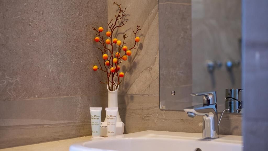Un baño con pared de mármol, un lavamanos con grifo moderno y una rama decorativa con flores naranjas y amarillas.