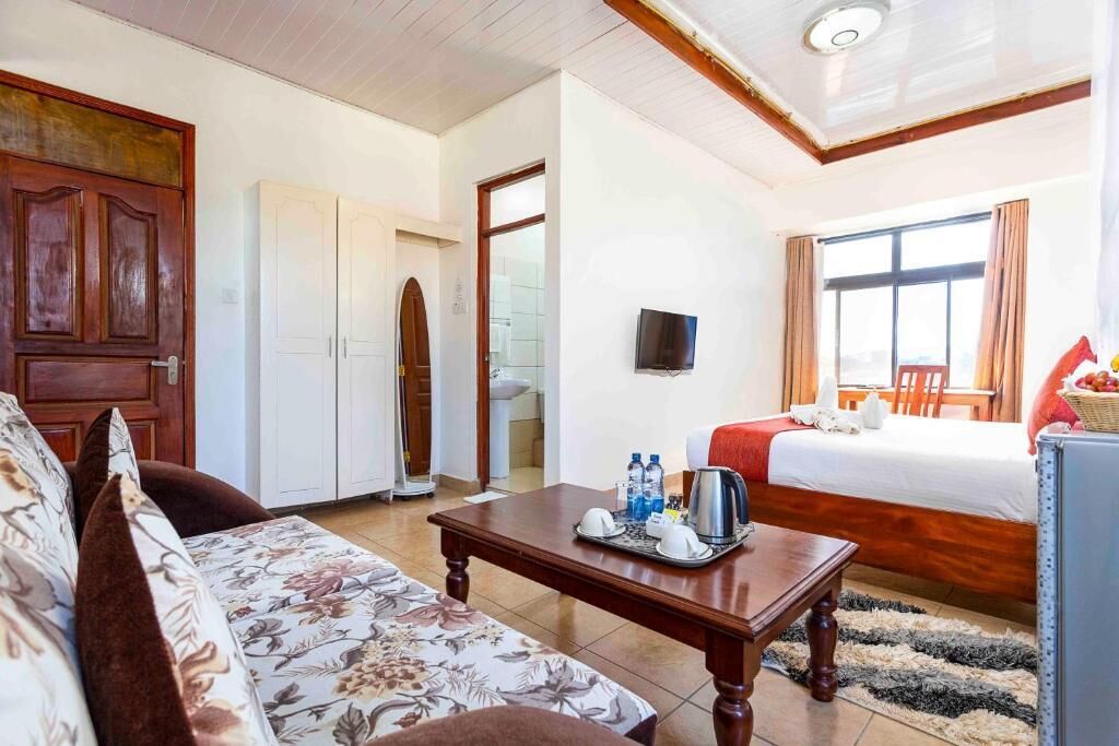 A room with a bed, a sofa, a television, and a table with amenities.