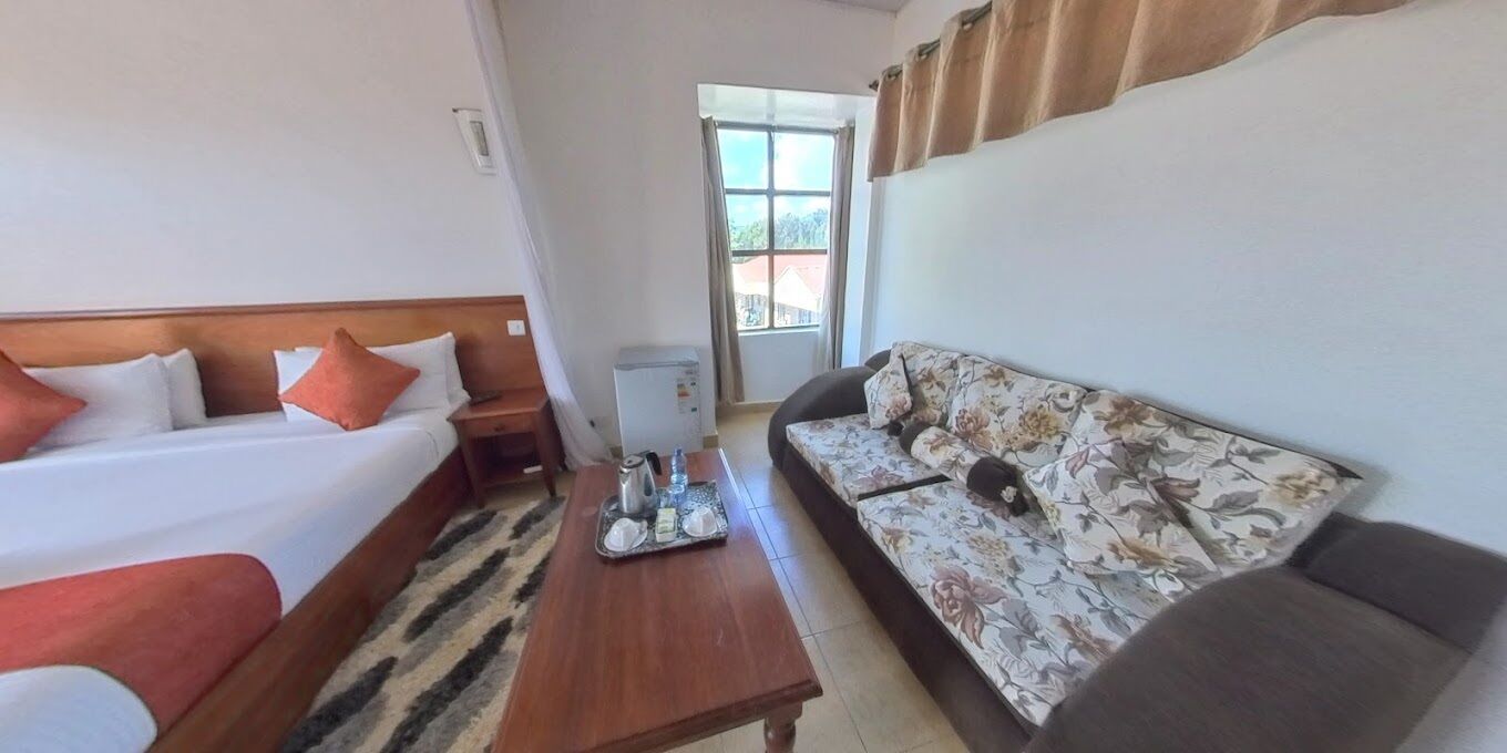 A hotel room with a bed, a sofa, a coffee table, and a window with curtains.