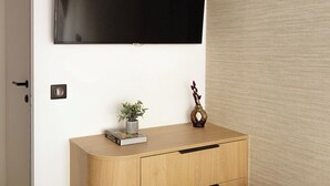Ein modernes Zimmer mit Flachbildfernseher an der Wand, einer Holzkabine mit Schubladen, einer kleinen Pflanze und einer dekorativen Vase.