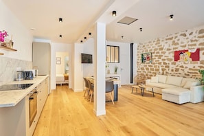 A modern kitchen with a marble countertop, wooden flooring, and a dining area with a white sofa and a stone wall. - Wonderful Apartment Center of Paris-montorgueil (Paris)