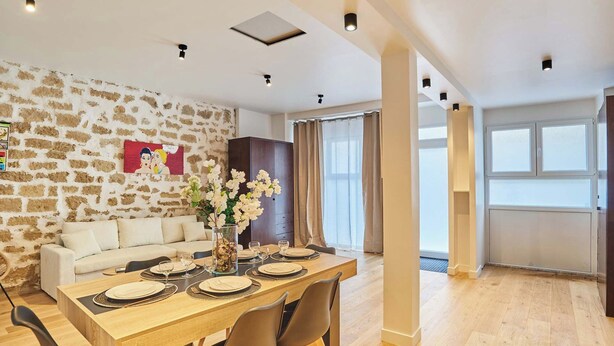 A modern living room with a stone wall, a sofa, a dining table set with plates and glasses, and a vase of flowers. - Wonderful Apartment Center of Paris-montorgueil (Paris)
