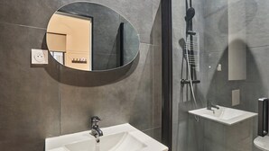 A modern bathroom with a large oval mirror, a rectangular sink, and a shower area. - Wonderful Apartment Center of Paris-montorgueil (Paris)