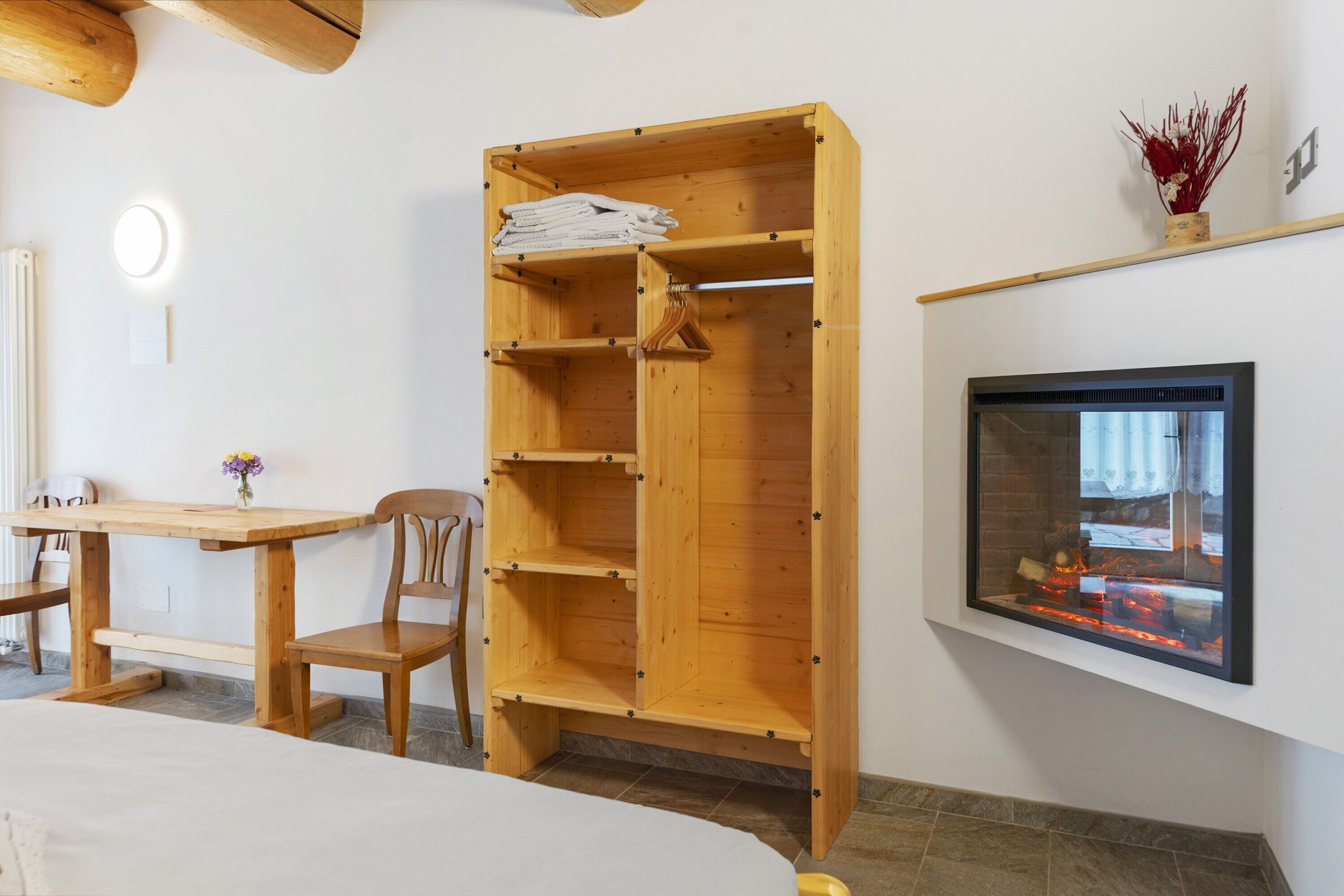 Una habitación con un armario de madera, una mesa con sillas, una chimenea y un televisor instalado en la pared.