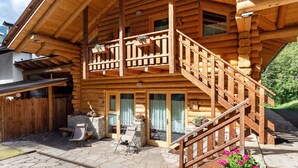 A wooden log cabin with a balcony, stone patio, and a staircase leading to the entrance. - 'Genziana' Room with Mountain View, Private Terrace and Wi-Fi (Cogolo di Peio)