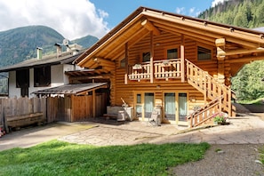 A wooden log cabin with a balcony, stone patio, and a view of mountains.