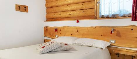 Una habitación estilo cabaña de madera con una cama, una ventana con cortinas de encaje y un cabecero de madera.
