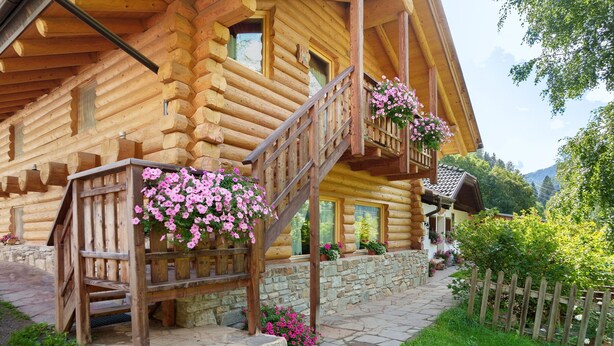 Una baita di legno con una scala in legno, gradini in pietra e cesti di fiori.