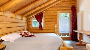A wooden cabin with a loft bedroom, a wooden bed, a window with curtains, and a door leading outside. - 'Primula' Room with Mountain View, Shared Garden and Wi-Fi (Cogolo di Peio)