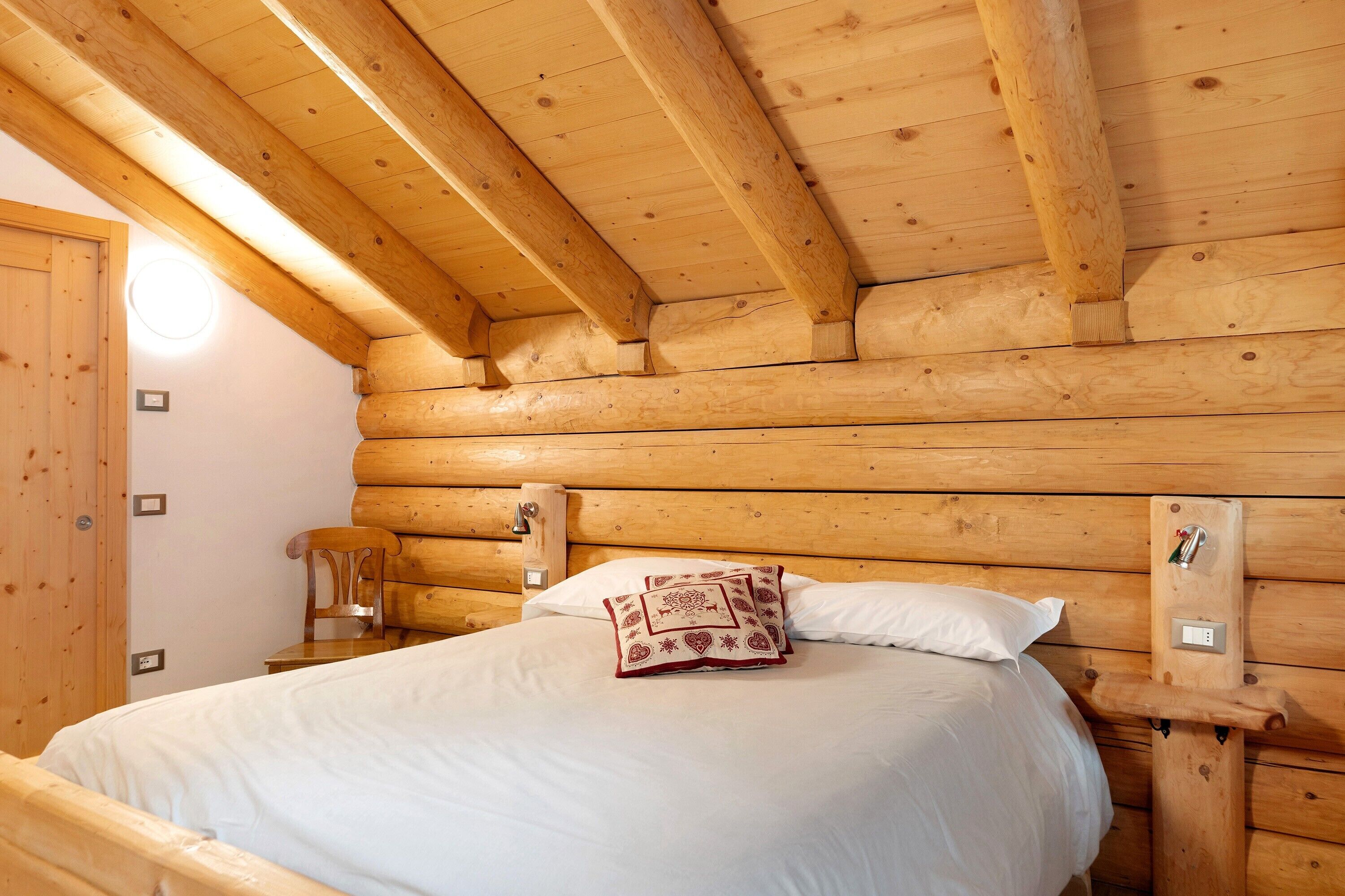 Une chambre à coucher située dans un chalet en rondins de bois, avec un lit, des oreillers, une table de chevet et une chaise en bois.