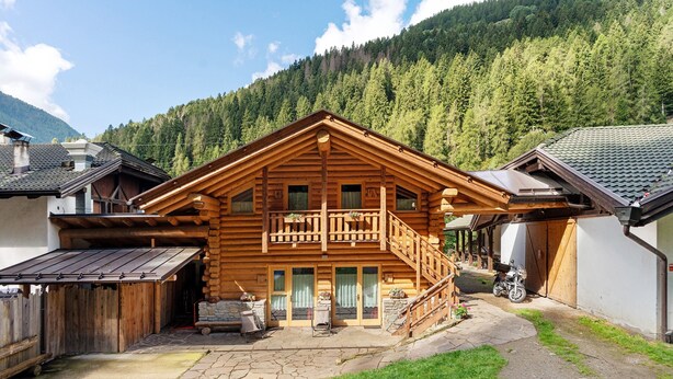 A wooden cabin with a balcony, stone patio, and a motorcycle parked outside. - Room 'Cazzuffi Rododendro' with Mountain View, Private Terrace and Wi-Fi (Cogolo di Peio)