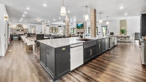Una cocina moderna con una isla grande, armarios oscuros y una zona de comedor con sillas blancas.