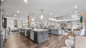 Una cocina amplia con una isla central, electrodomésticos modernos y un comedor con techo alto y paredes de ladrillo visto.