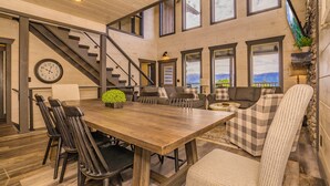 A spacious living area with a wooden dining table, multiple seating options, a staircase, and large windows offering views. - Fantastic View|Theater|Indr Pool|Pool Table|HotTub (Sevierville)