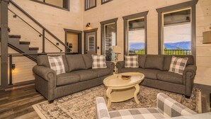 A spacious living room with two grey sofas, a coffee table, and a patterned rug. A staircase is visible in the background. - Fantastic View|Theater|Indr Pool|Pool Table|HotTub (Sevierville)