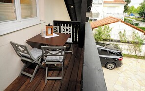 Een balkon met een tafel en stoelen, een geparkeerde auto buiten en uitzicht op de straat en gebouwen.