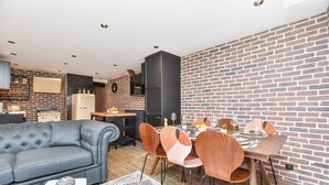 A modern living room with a grey sofa, dining table with wooden chairs, and a brick wall. - Charming 3BR Apt- Montorgueil / Republique (Paris)
