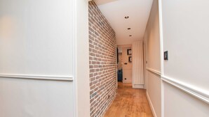 A narrow hallway with a brick wall on one side and white walls on the other, leading to a room with a door. - Charming 3BR Apt- Montorgueil / Republique (Paris)