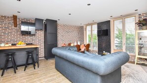 A modern kitchen with a brick wall, a wooden countertop, and a built-in oven. There is a grey sofa and two black stools in the living area. - Charming 3BR Apt- Montorgueil / Republique (Paris)