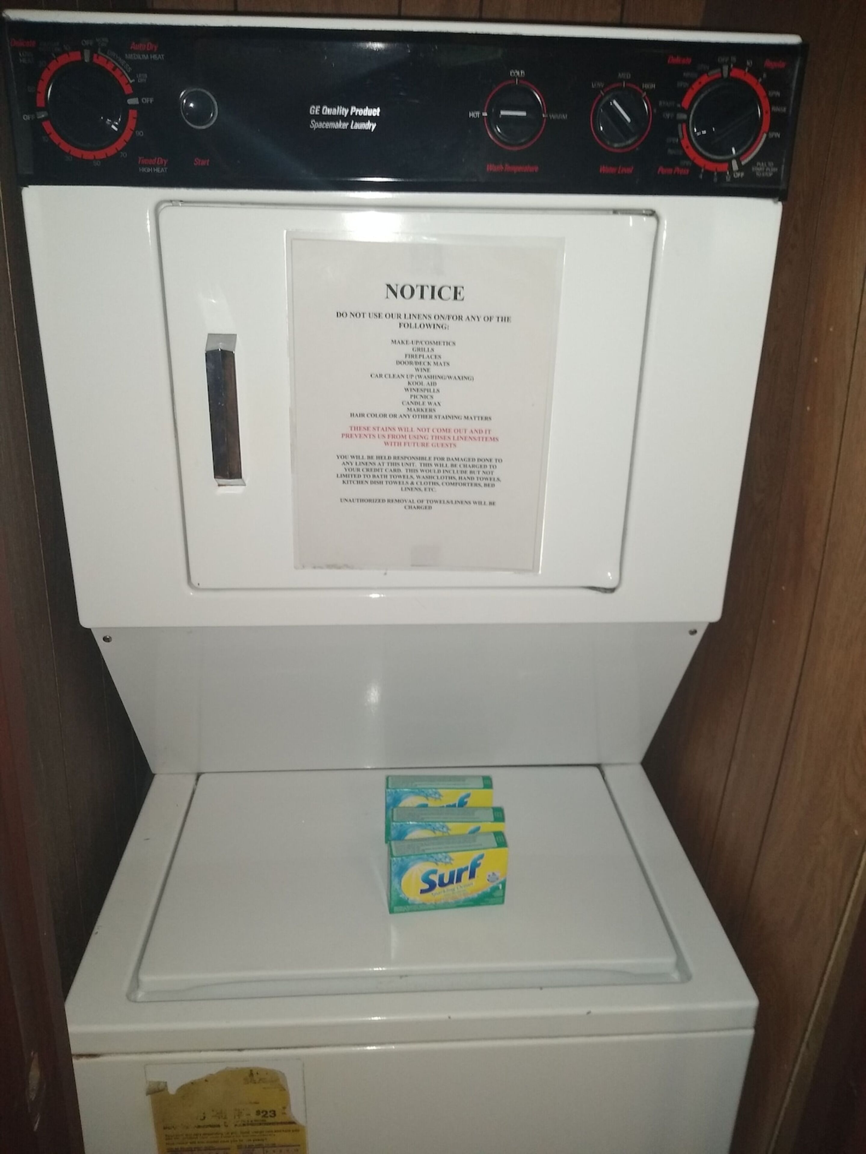 A front-loading washing machine with a notice taped to the door warning against using the machine for certain items.