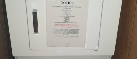 A front-loading washing machine with a notice taped to the door warning against using the machine for certain items.