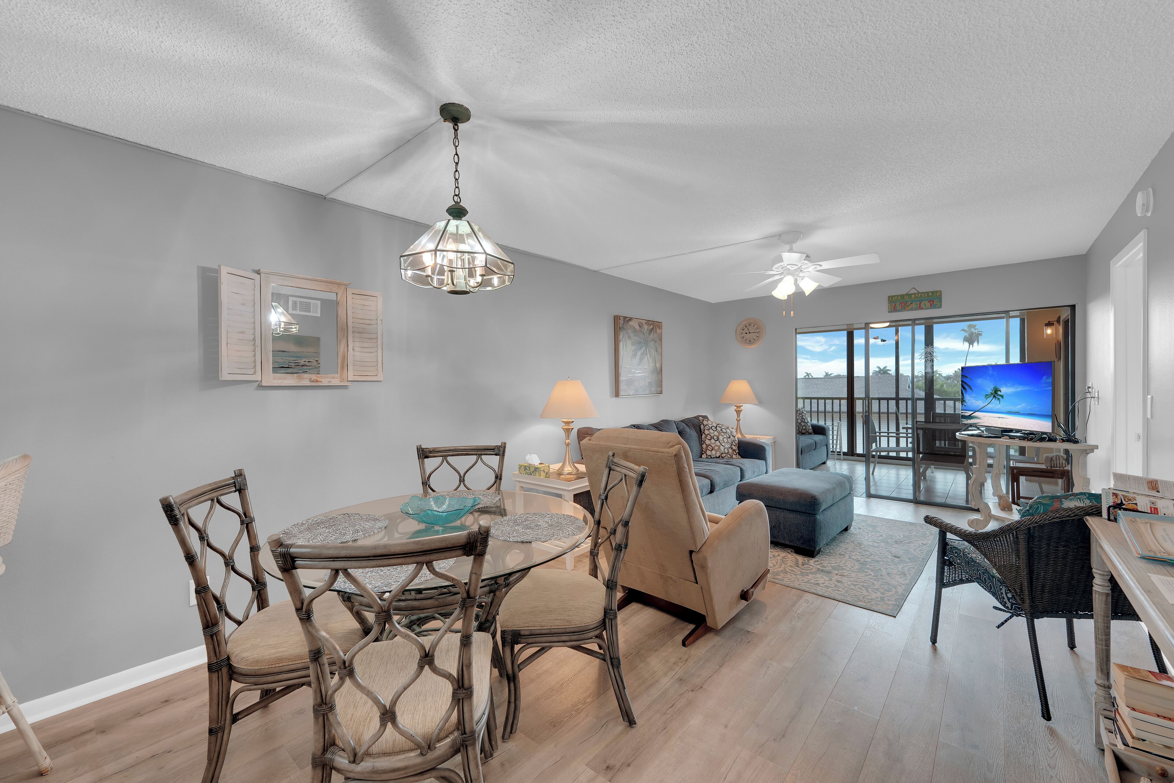 A spacious living area with a dining table, chairs, and a sofa. There is a television and a large window with a view of the outdoors.
