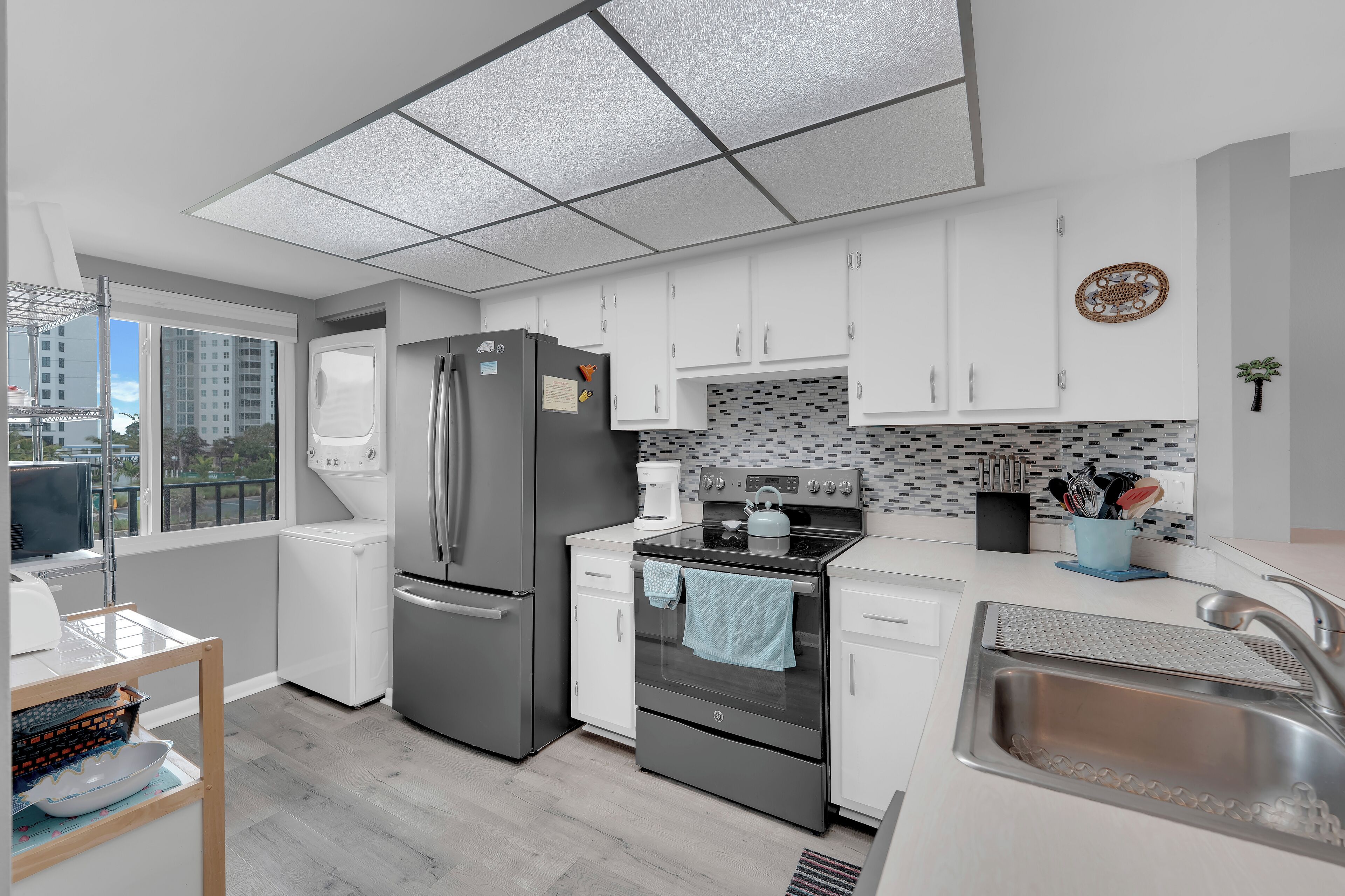 A modern kitchen with white cabinets, a stainless steel refrigerator, an oven, and a sink.