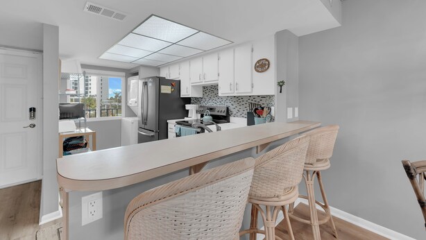Une cuisine moderne avec des meubles blancs, un grand îlot central doté de tabourets et une vue sur la ville.