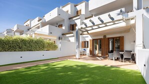 A modern white building with balconies, a patio area with outdoor furniture, and a well-maintained lawn.