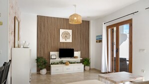 A modern living room with a flat-screen TV, a woven pendant light, a wooden slatted wall, and a sliding glass door leading to an outdoor area.