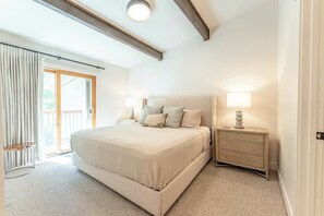 A bedroom with a large bed, two bedside tables with lamps, a sliding glass door to a balcony, and a ceiling with exposed beams. - Oak at Outrun, brand new remodel, fireplace! (Mt. Crested Butte)