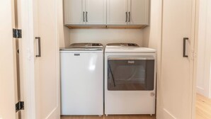 A small laundry room with two white appliances, a dryer and a washing machine, under white cabinets. - Oak at Outrun, brand new remodel, fireplace! (Mt. Crested Butte)