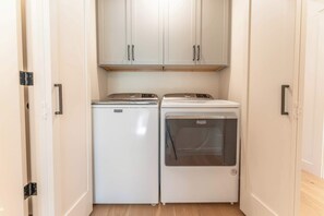 A small laundry room with two white appliances, a dryer and a washing machine, under white cabinets. - Oak at Outrun, brand new remodel, fireplace! (Mt. Crested Butte)