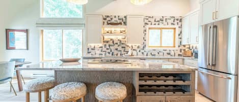 A modern kitchen with a large island, bar stools, wine storage, and stainless steel appliances.