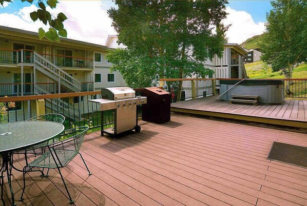A deck with a grill, a table with chairs, and a trash can.