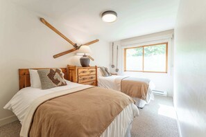 A bedroom with two beds, a wooden headboard, a lamp, and a window.