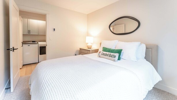 A bedroom with a bed, a nightstand, a mirror, and a kitchenette in the background. - Oak at Outrun, brand new remodel, fireplace! (Mt. Crested Butte)