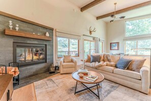 A cozy living room with a fireplace, a sofa, a coffee table, and a view of the outdoors.