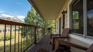 A wooden deck with a view of mountains and a building in the distance. - Oak at Outrun, brand new remodel, fireplace! (Mt. Crested Butte)