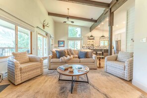 A spacious living room with a large sofa, two armchairs, a coffee table, and a fireplace. There are large windows providing natural light and a view of the outdoors. - Oak at Outrun, brand new remodel, fireplace! (Mt. Crested Butte)