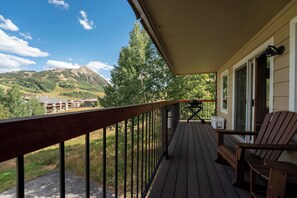 Una terraza de madera con vista a montañas y un edificio al fondo.