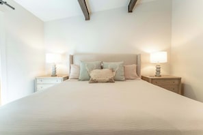 A neatly made bed with a headboard, two bedside tables with lamps, and a light-colored wall.