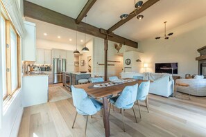 A spacious kitchen with modern appliances, a dining area with a wooden table and blue chairs, and a living area with a sofa and TV.