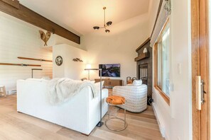 A modern living room with a white sofa, a round coffee table, a fireplace, and skis on the wall. - Oak at Outrun, brand new remodel, fireplace! (Mt. Crested Butte)