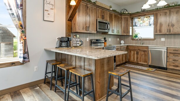 A kitchen with wooden cabinets, a central island with stools, a microwave, and a dishwasher. - Secluded Wine Retreat | Game Room | Sauna/Firepit (Penn Yan)