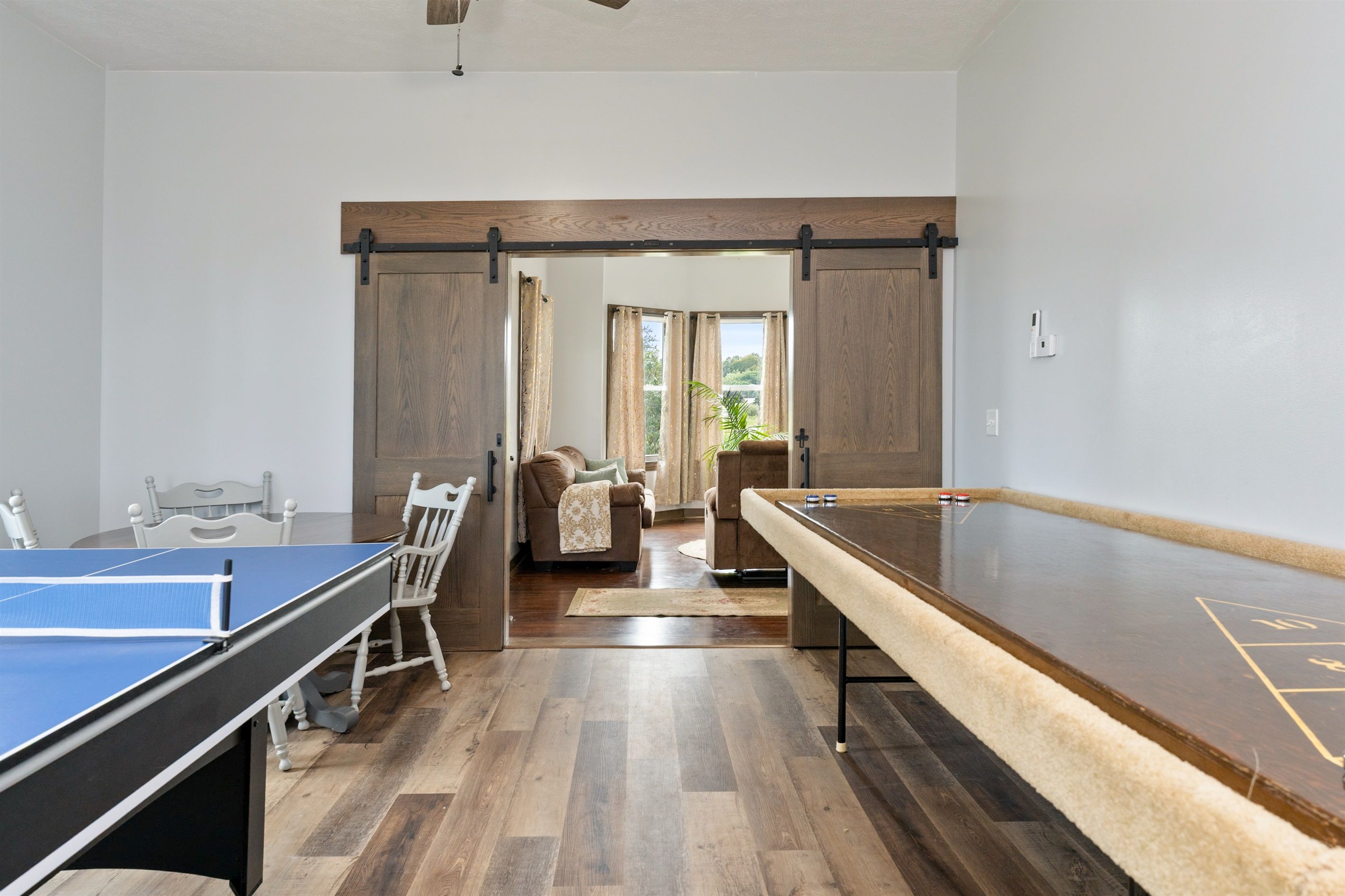 A room with a ping pong table, a shuffleboard table, and a dining table with chairs.