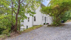 Une maison blanche avec une allée en gravier, entourée d’arbres et de verdure.